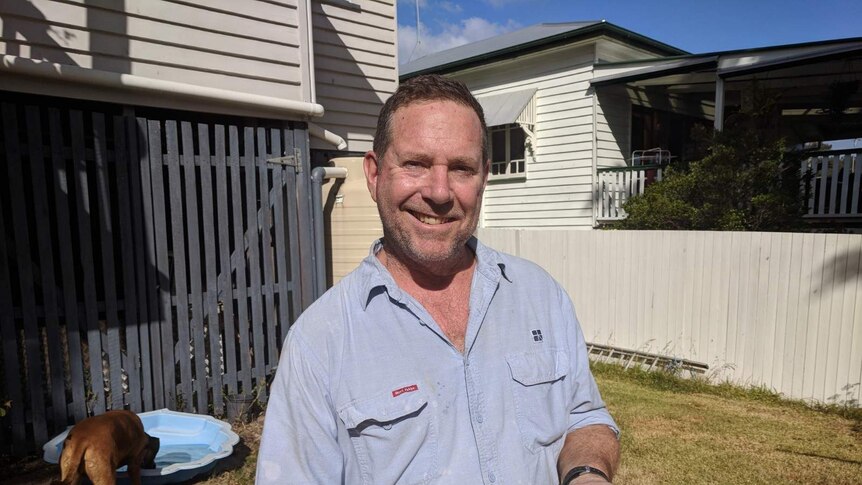 Man standing in a suburban backyard, smiling, holding three eggs