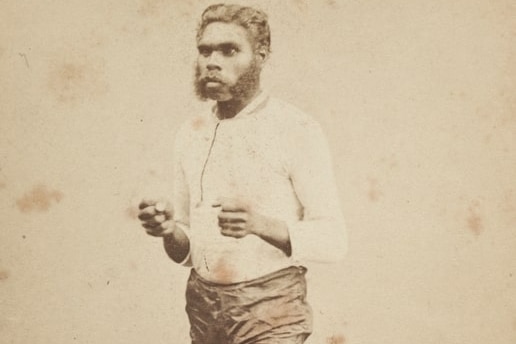 An old photo of an Indigenous man standing with his fists clenched