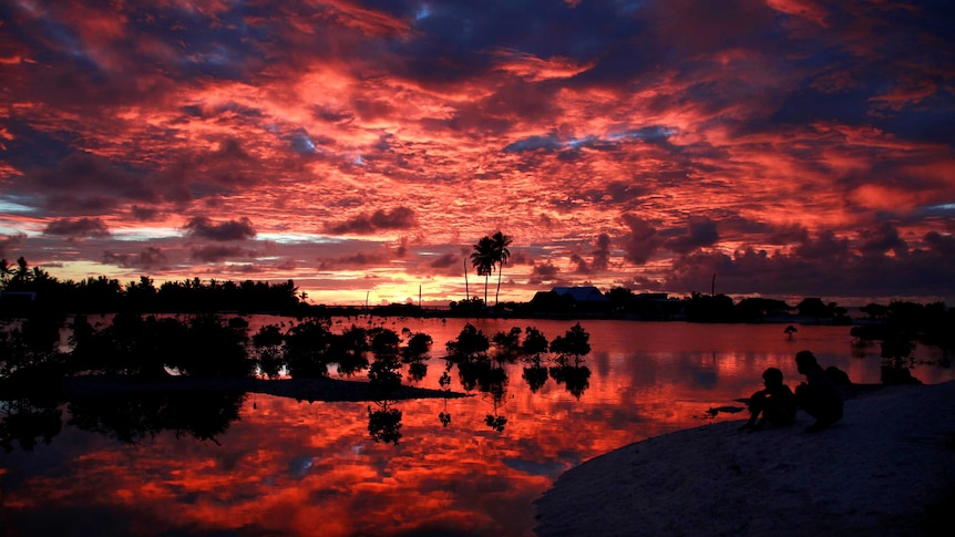 Villagers watch the sunset over a small lagoon in Kiribati.