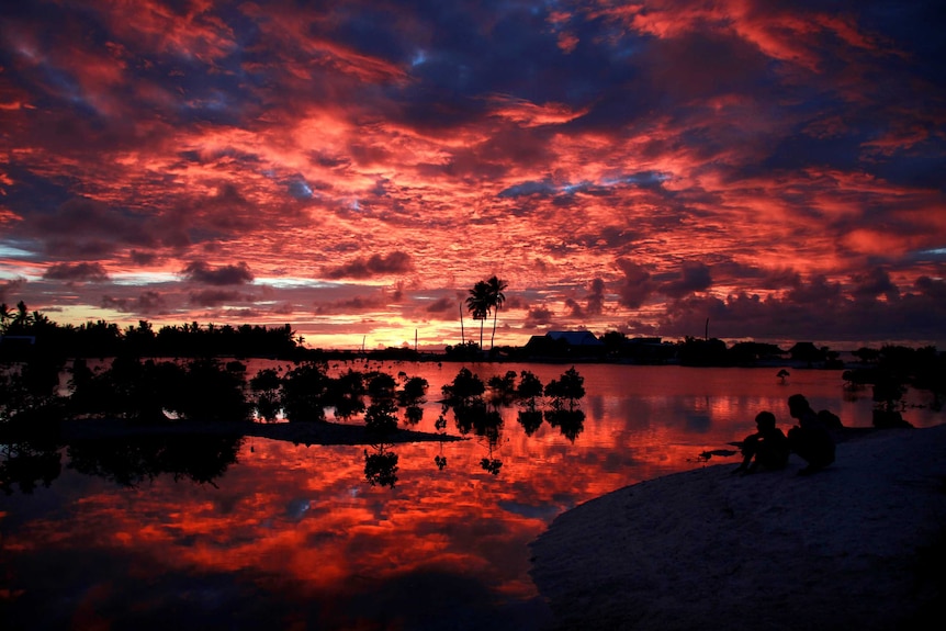 Villagers watch the sunset over a small lagoon in Kiribati.