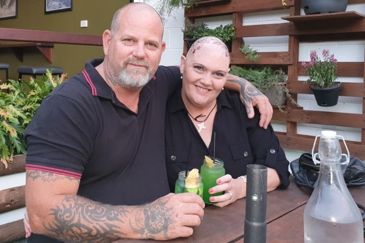 Will Barabas and Katrina Mears sitting down and smiling with their arms around each other, holding green drinks.