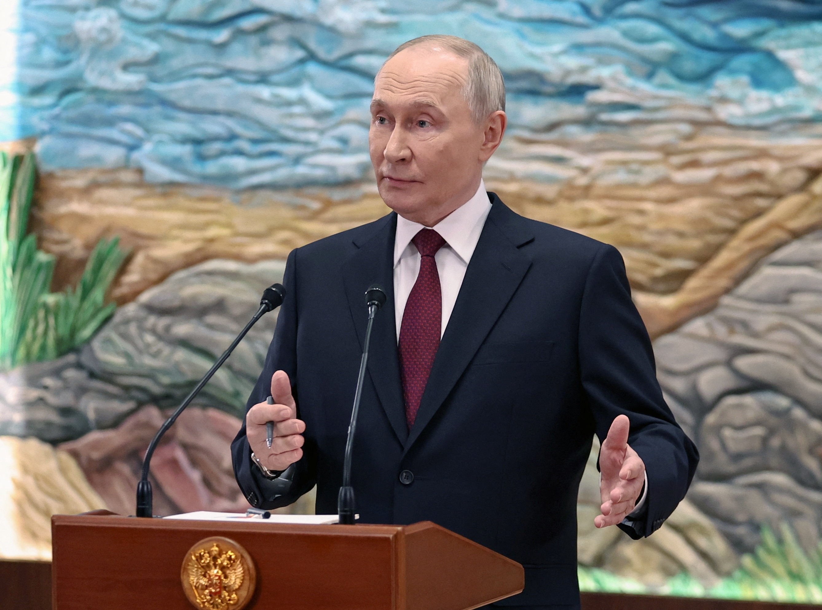 A man wearing a suit speaks at a podium. 
