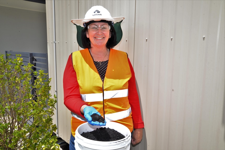 A woman wearing high-vis clothes holds a handful of black charcoal
