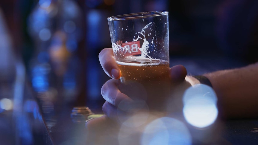 A man's hand holds a beer in a bar.