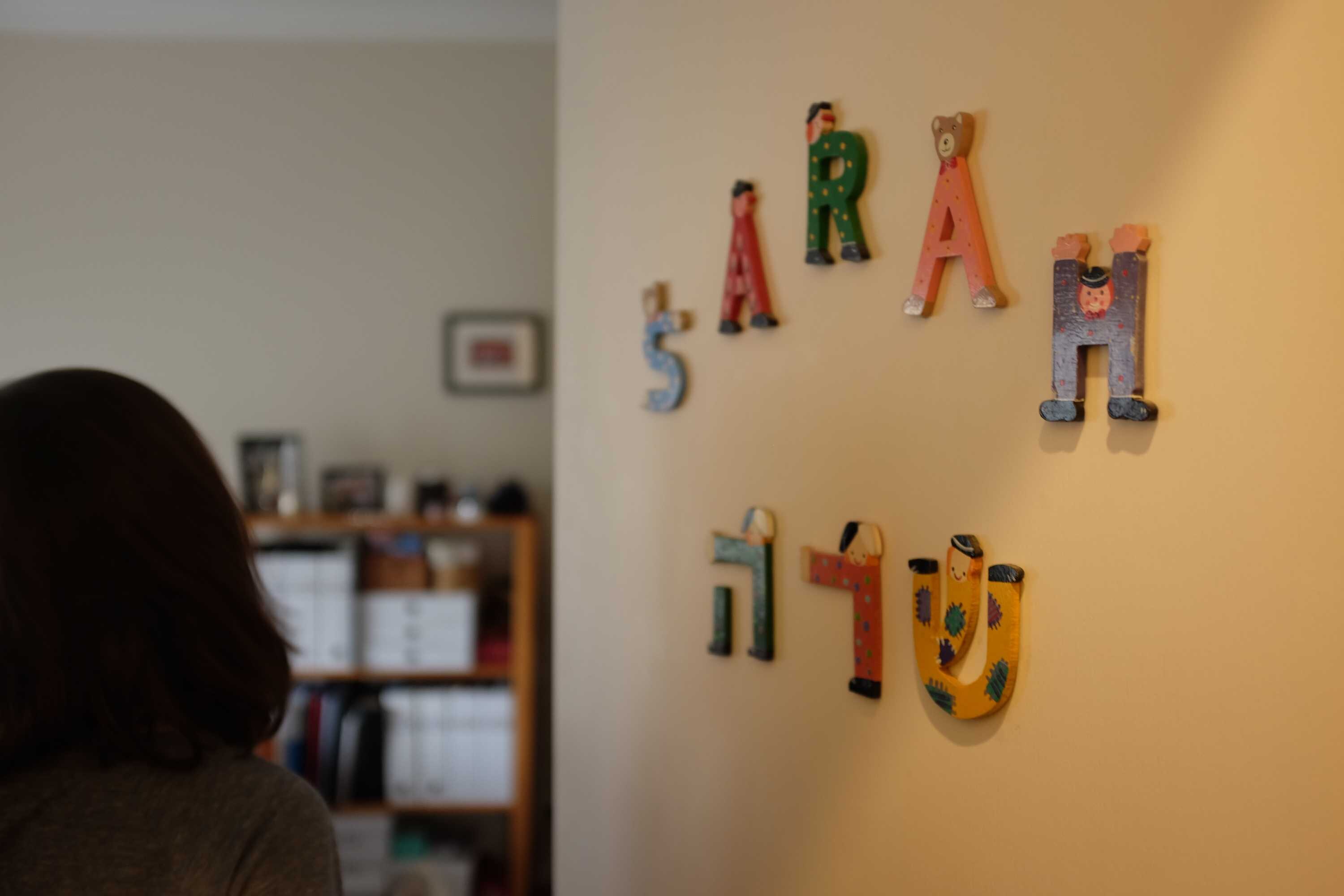 自分の部屋に入る女性。ドアには木製の置物で自分の名前「サラ」が飾られている。