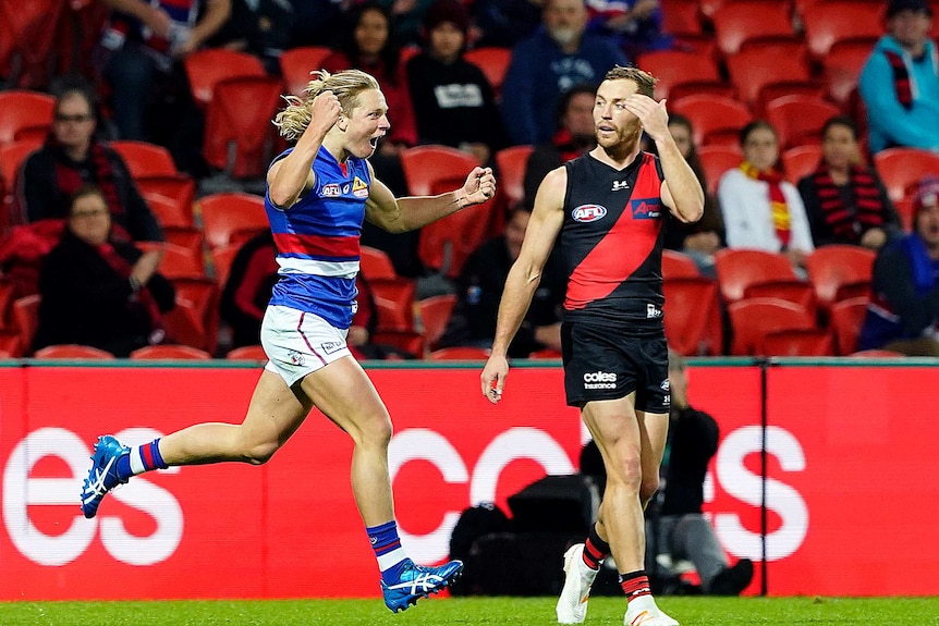 An AFL player runs back with his arms raised in triumph after kicking a goal.