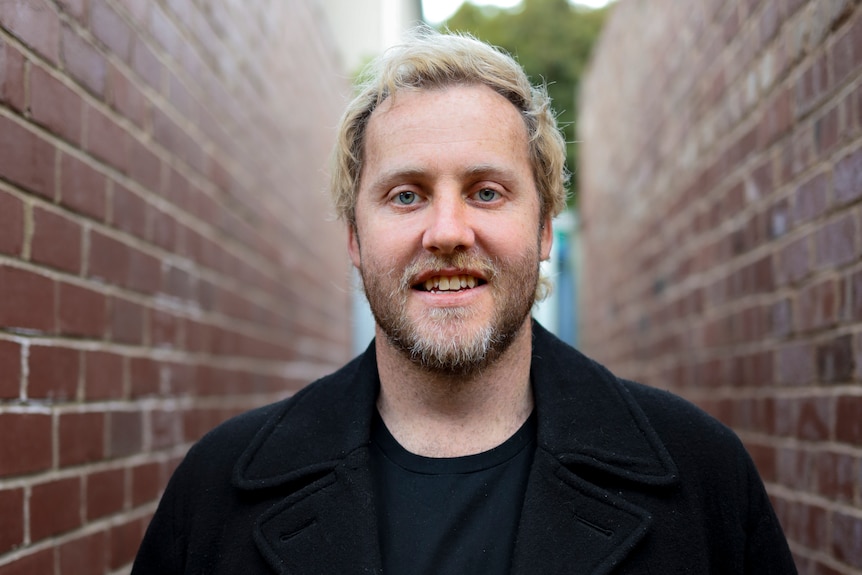 Man with blonde hair and beard smiling at camera.