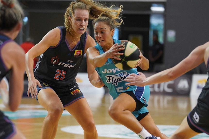 A Southside Flyers WNBL player drives to the basket while being defended against by the Townsville Fire.
