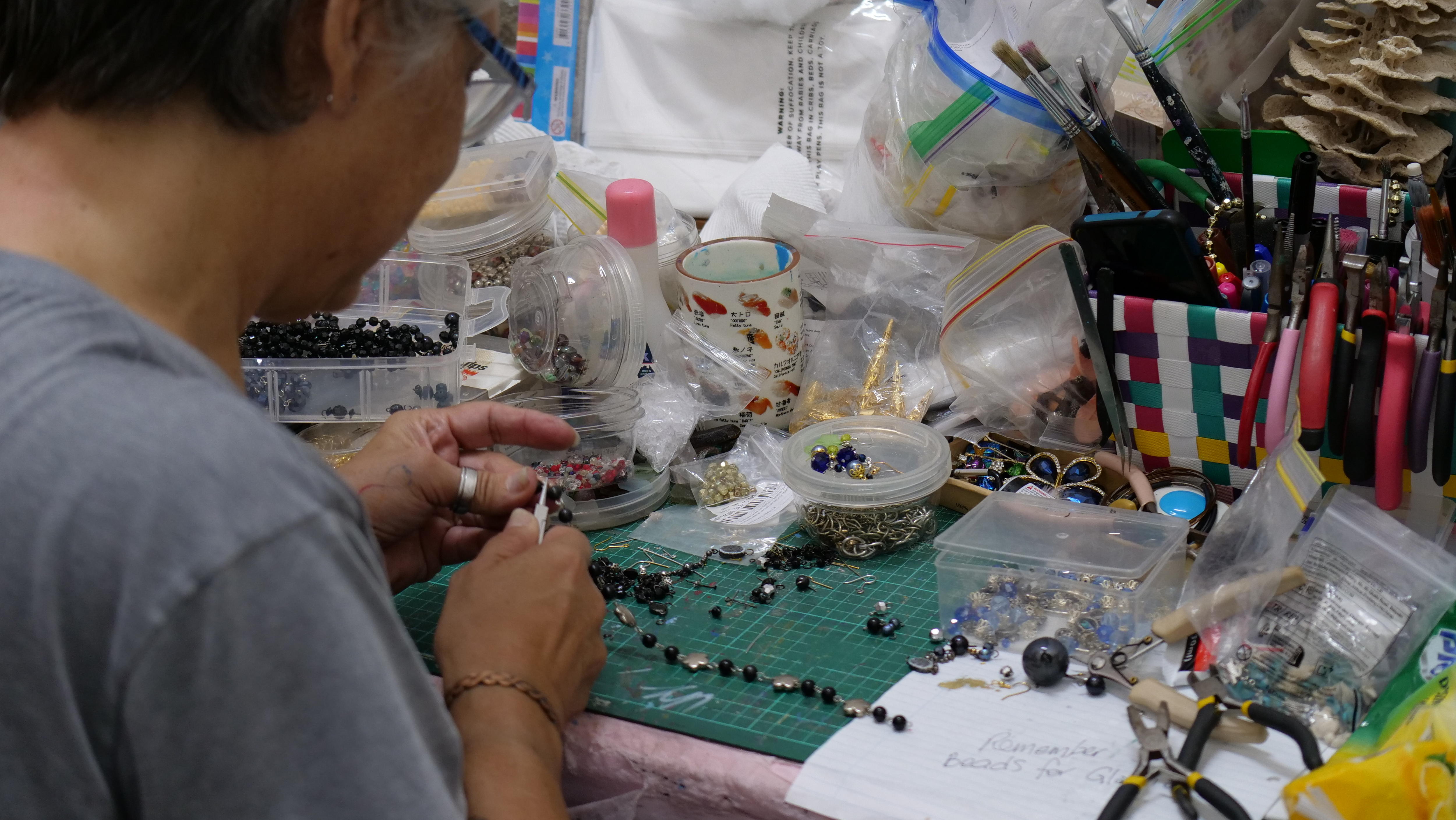 Uma mesa coberta de miçangas e uma mão segurando ferramentas. 