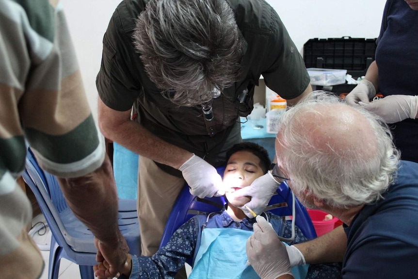 A volunteer holds the hand of a young East Timorese boy while he receives dental treatment in Dili.