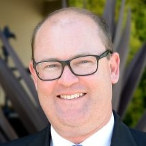 A bald man with spectacles smiles for the camera