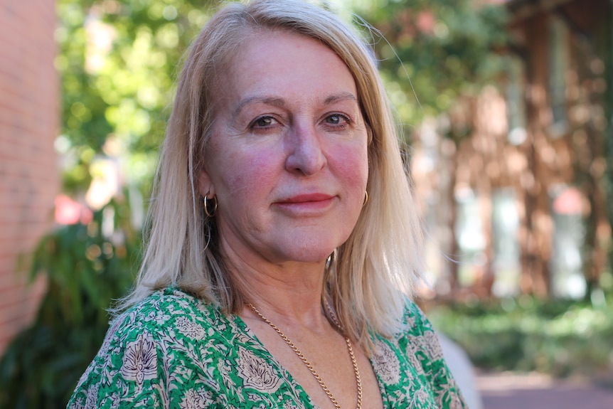 A portrait photo of a woman with blonde hair wearing a green patterned top.