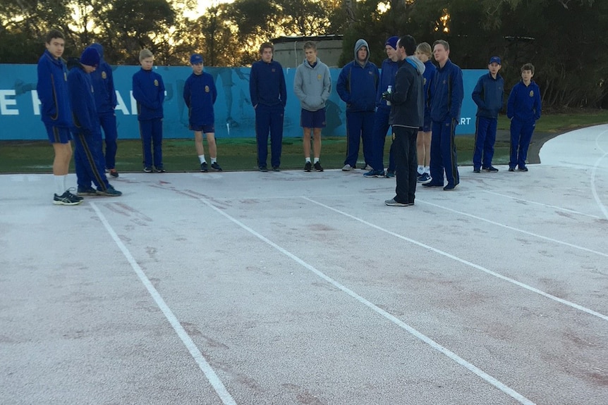 Schoolboys look over the frosty running track on cold August morning.