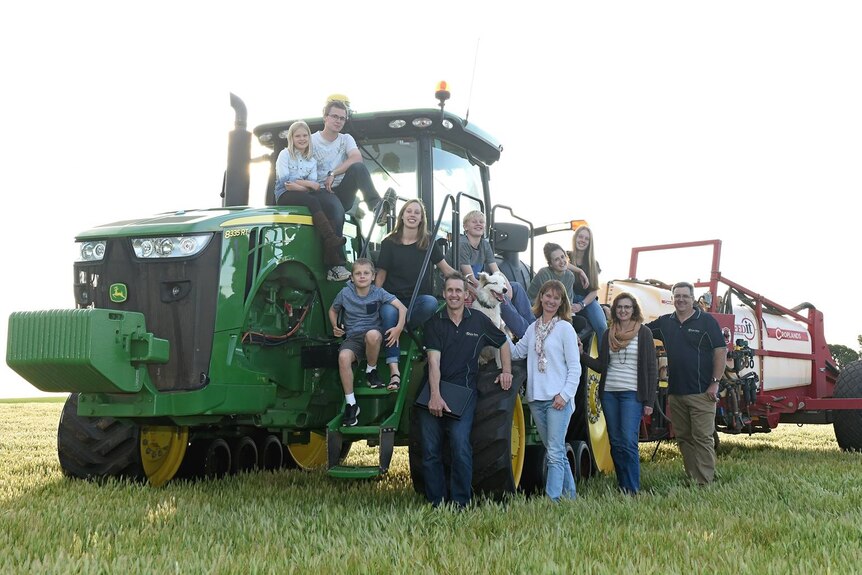 A group of people standing around a tractor, smiling.
