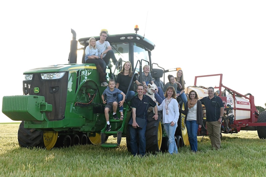 A group of people standing around a tractor, smiling.