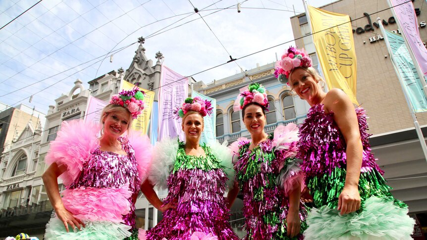 Four women in bright outfits stare at the camera.
