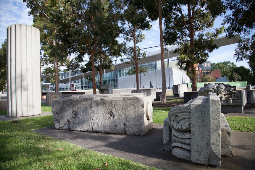 Large stone blocks on display as sculptures, with trees and a museum in the background.