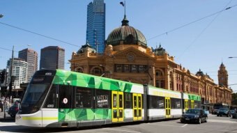 A tram moves past the front of Flinders Street Station on a sunny day.