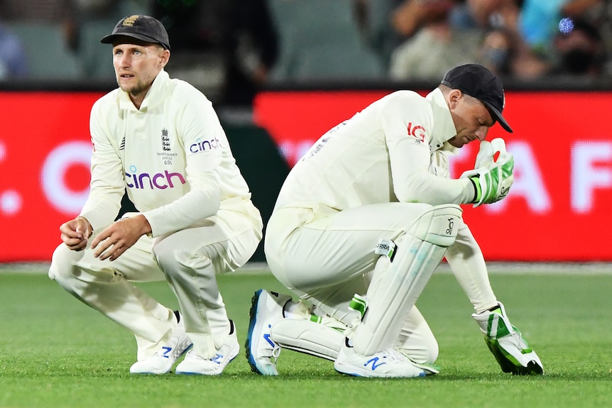 Jos Buttler holds his head in his hand and Joe Root squats next to him with a pained expression on his face