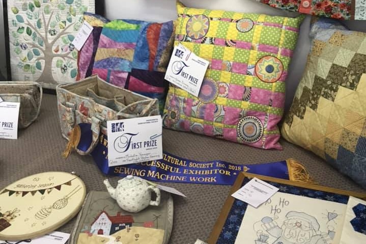 A table filled with quilt, pillow and craft work to be judged as part of a competition