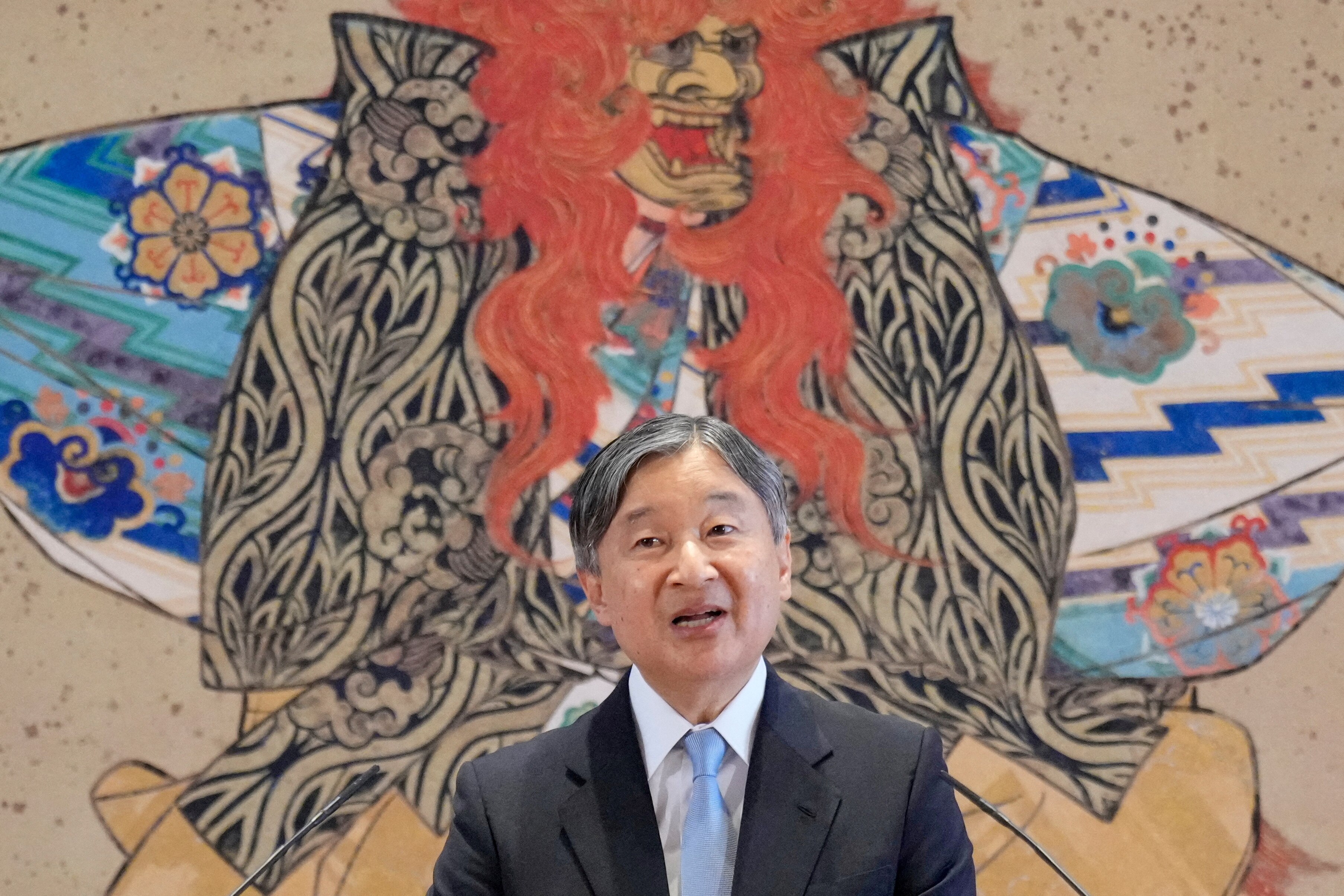 Un hombre habla durante una conferencia de prensa frente a una pintura tradicional japonesa.