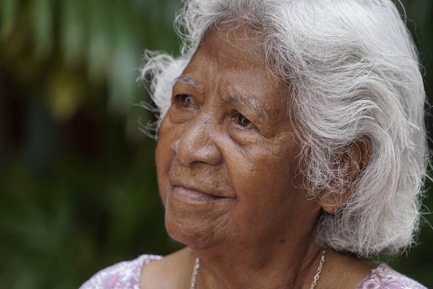 A woman with white hair stares into the distance. 