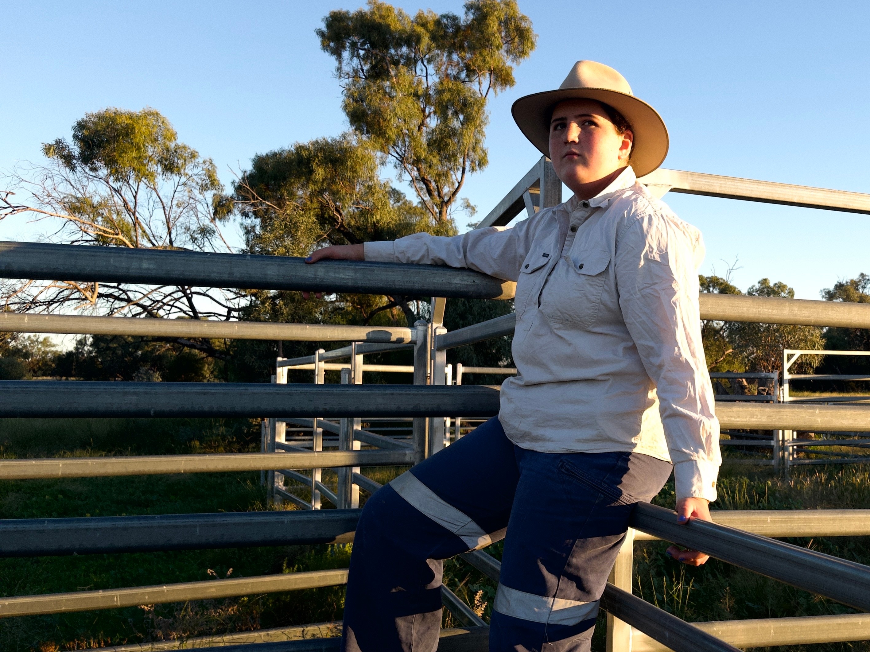 A teenage girl sits on a farm fence.