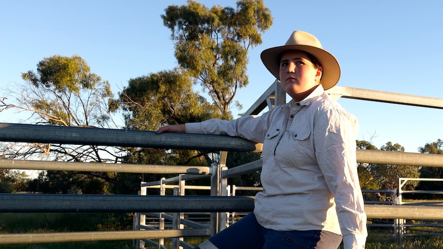 A teenage girl sits on a farm fence.