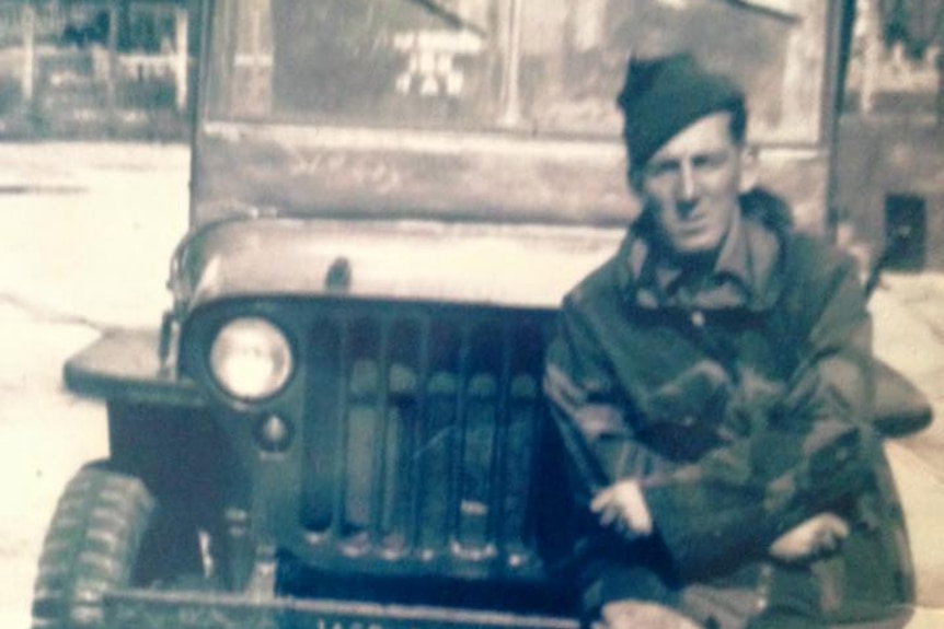 Grainy and sepia-coloured image of young soldier learning against the bumper of a small military jeep