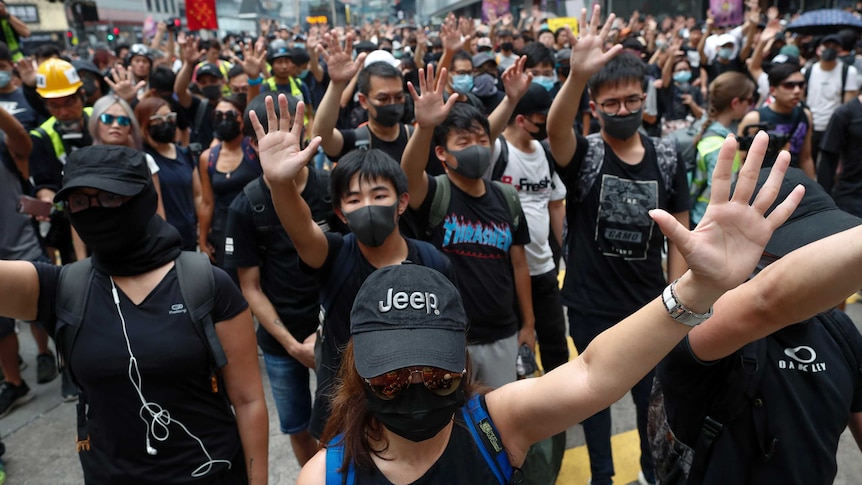 Protesters wear black clothes and hold their hands out as they march