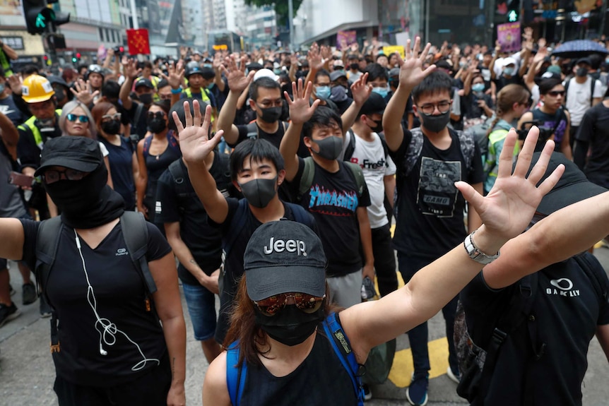 Protesters wear black clothes and hold their hands out as they march