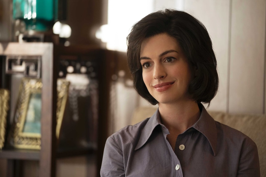 The actor Anne Hathaway with a dark bob and a tentative smile in a lounge room in the movie Dark Waters