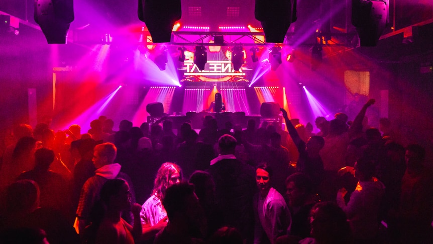 A crowded dance floor in a nightclub, with bright pink and red light beams.