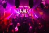 A crowded dance floor in a nightclub, with bright pink and red light beams.