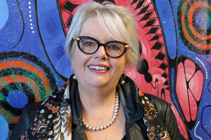 Gail Middleton wears glasses and stands in front of purple mural wall.