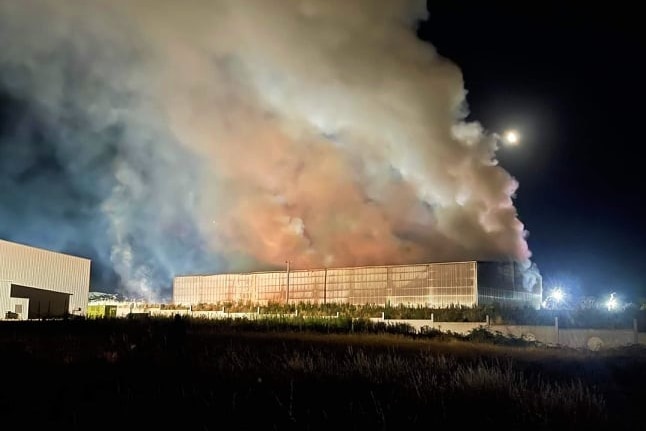 A warehouse burns with smoke filling the night sky.