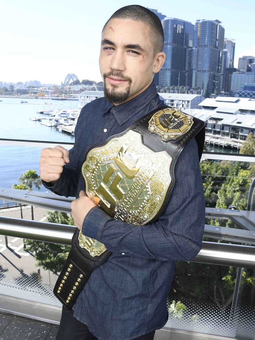 Robert Whittaker with the UFC middleweight belt held on his shoulder.