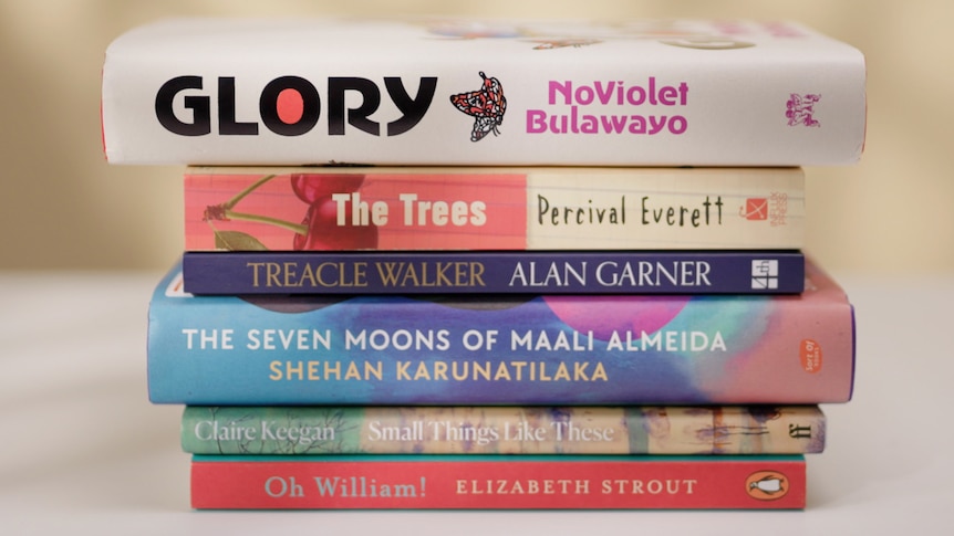 A stack of six books, of various sizes and lengths, as well as different colours, such as red, white and navy