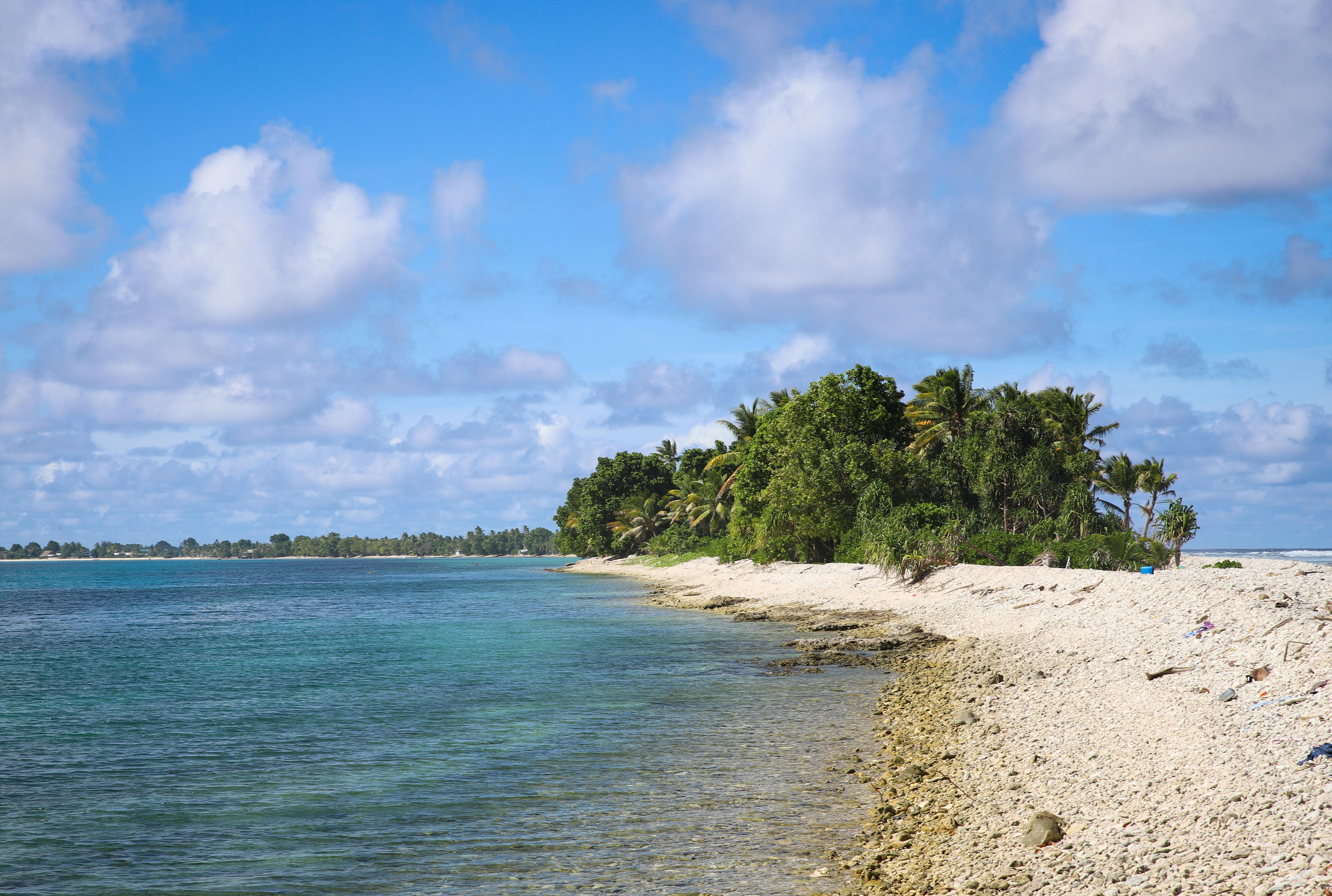 A blue lagoon sits on the left of the image, with a narrow strip of land stretching away, covered in palm trees.