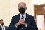 President Joe Biden speaks to the media wearing a black face mask.