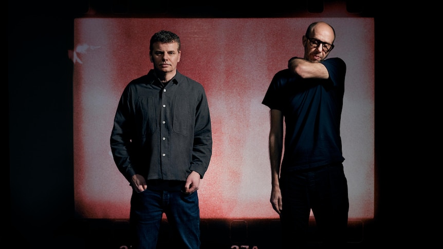 The Chemical Brothers' two members stand and pose against a white-red soundstage