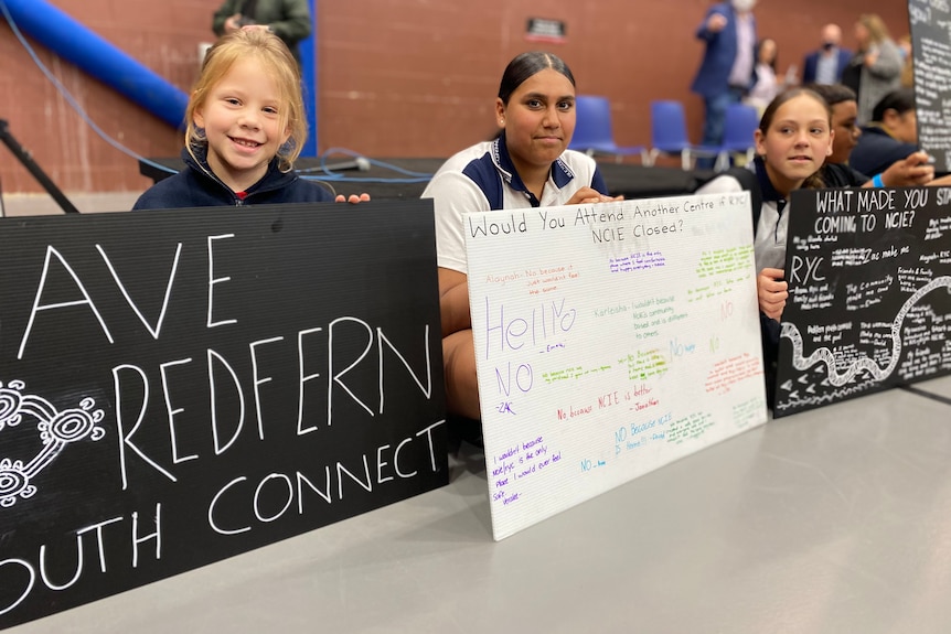 a number of young students sitting on the floor holding signs