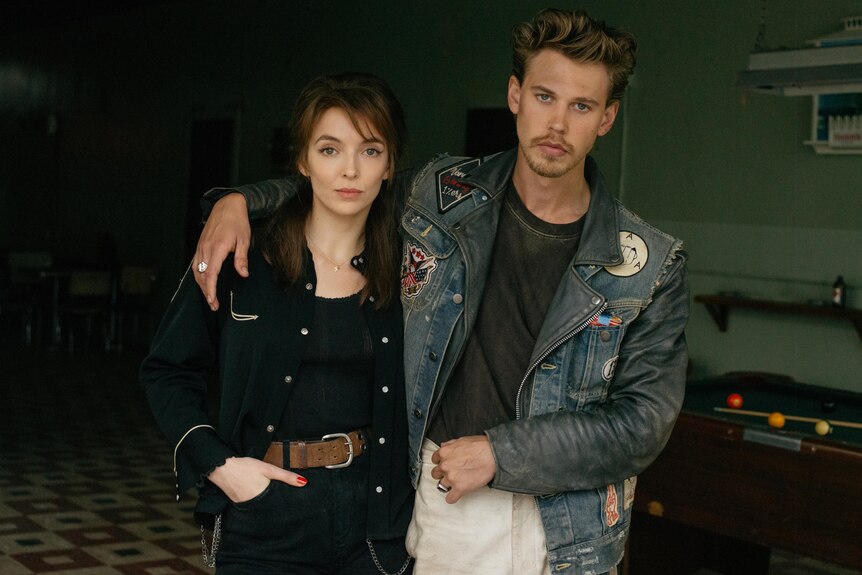 Jodie Comer and Austin Butler in leather jackets, his arm around her shoulder