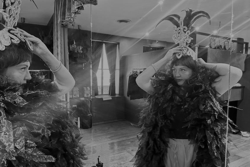Victoria Brooke looks at herself in the mirror while putting on a feather head piece. 