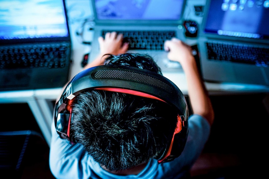 A child wearing a headset sits in front of computer screens