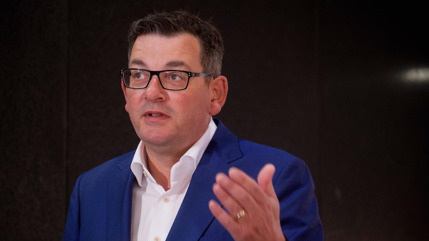 Daniel Andrews, in a white shirt and blue jacket, speaks to reporters outside.