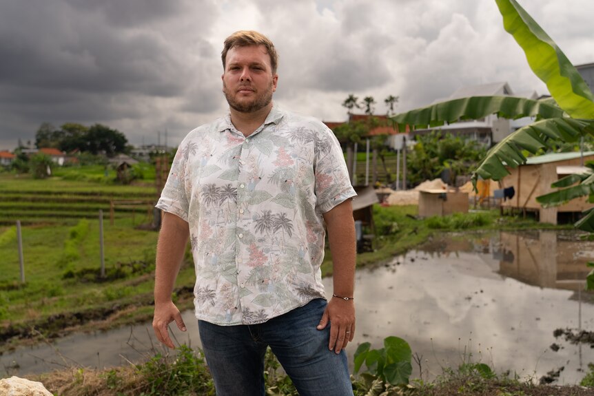 A blonde man in a tropical shirt stands in a rice paddy field 