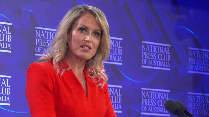 A lawyer with long blonde hair in red sleeved dress with purple backdrop 