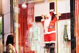 A woman looks at a shop window which shows a Santa Claus on a crucifix.