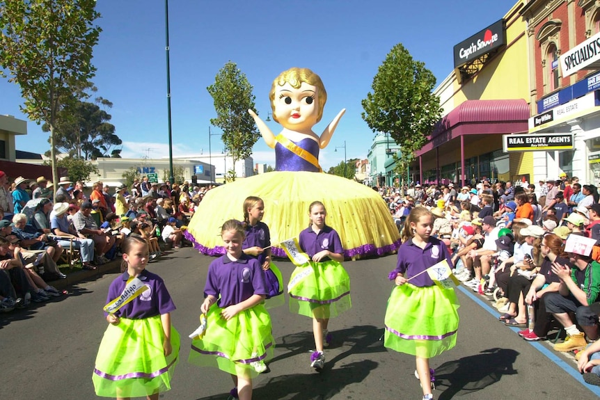 Giant kewpie doll in street parade with children in foreground